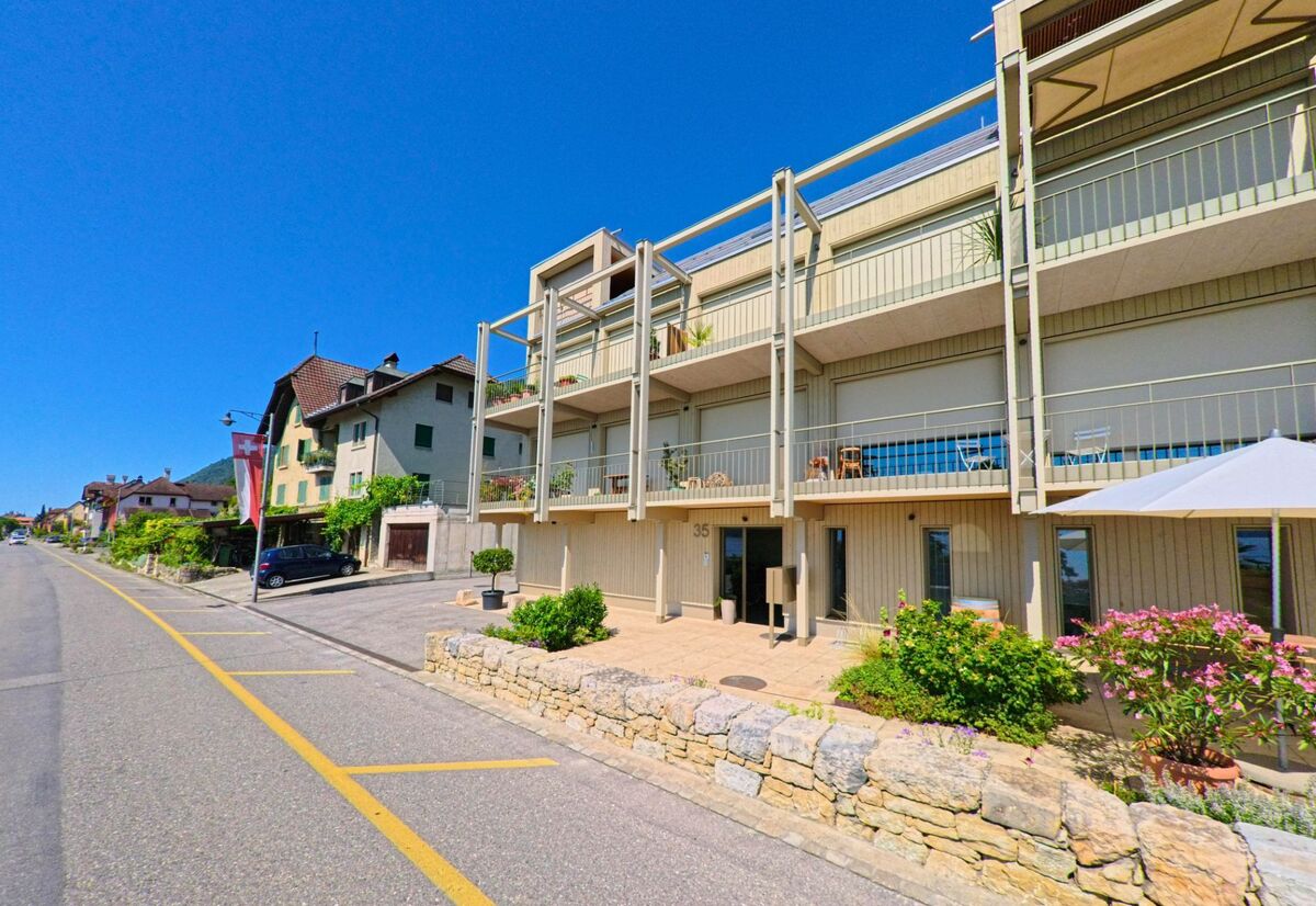 In Ligerz (2514, Kanton Bern) steht ein modernes Wohngebaeude mit grossen Balkonen neben traditionellen Haeusern an der Hauptstrasse.