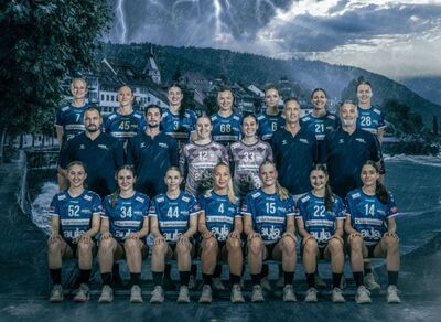 In Zug (6343, Kanton Zug) posiert das Team von LK Zug Handball in blauen Trikots vor einer dramatisch inszenierten Hintergrundkulisse mit Gewitter und Altstadtmotiven.