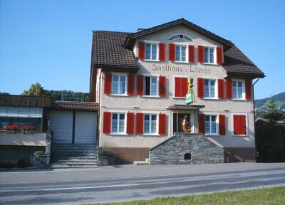 Beim Restaurant Löwen in Kaltbrunn (8722, Kanton St. Gallen) leuchten abends ein Windmuehlenmodell und ein kleines Chalet in warmer Beleuchtung.