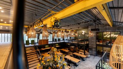 Die Loft 99 Eventlocation in S-chanf (7525, Kanton Graubuenden) zeigt einen grosszuegigen Saal mit modernen Holzlampen, langen Tischen und industriellem Design.