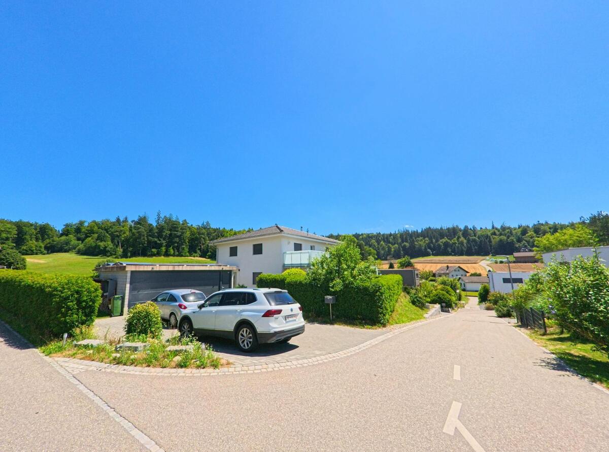Am Ortsrand von Lotzwil (4932, Kanton Bern) grenzen moderne Einfamilienhaeuser mit Carports an offene Felder und einen bewaldeten Hang.
