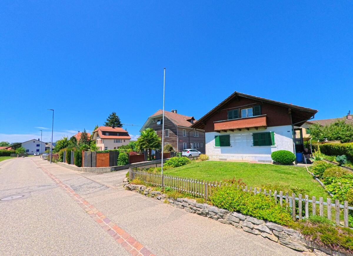 Ein Einfamilienhaus mit gruener Fensterlaeden und Vorgarten steht in Lotzwil (4932, Kanton Bern) entlang einer ruhigen Quartierstrasse mit weiteren Wohnhaeusern.