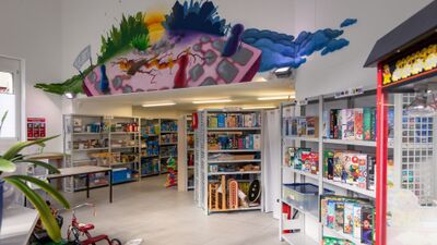 In der Ludothek Bülach in Bülach (8180, Kanton Zürich) stehen zahlreiche Gesellschaftsspiele und Spielmaterialien ordentlich in Regalen, während ein farbiges Wandbild den Raum belebt.