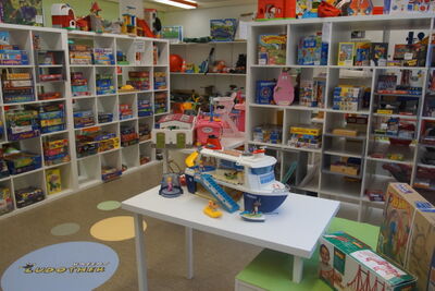 In einem hellen Raum der Ludothek in Kriens (6010, Kanton Luzern) stehen zahlreiche Spiele und Spielzeuge geordnet in Regalen sowie auf einem zentralen Tisch.