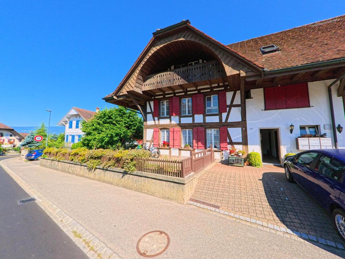 In Lüscherz (2576, Kanton Bern) steht ein traditionelles Fachwerkhaus mit rotem Fensterladen und überdachtem Balkon an einer Nebenstrasse.
