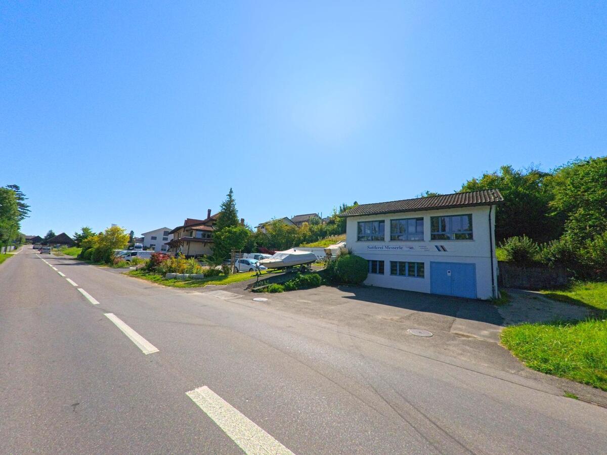 In Lüscherz (2576, Kanton Bern) steht ein Gewerbegebäude mit blauen Toren und Booten auf Anhängern neben einer Strasse am Dorfrand.