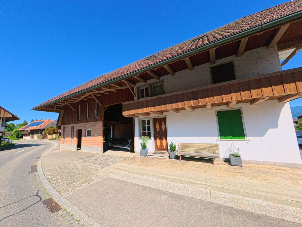 In Lüscherz (2576, Kanton Bern) steht ein grosses Wohn- und Wirtschaftsgebäude mit Holzbalkon an einer sanft gebogenen Strasse.