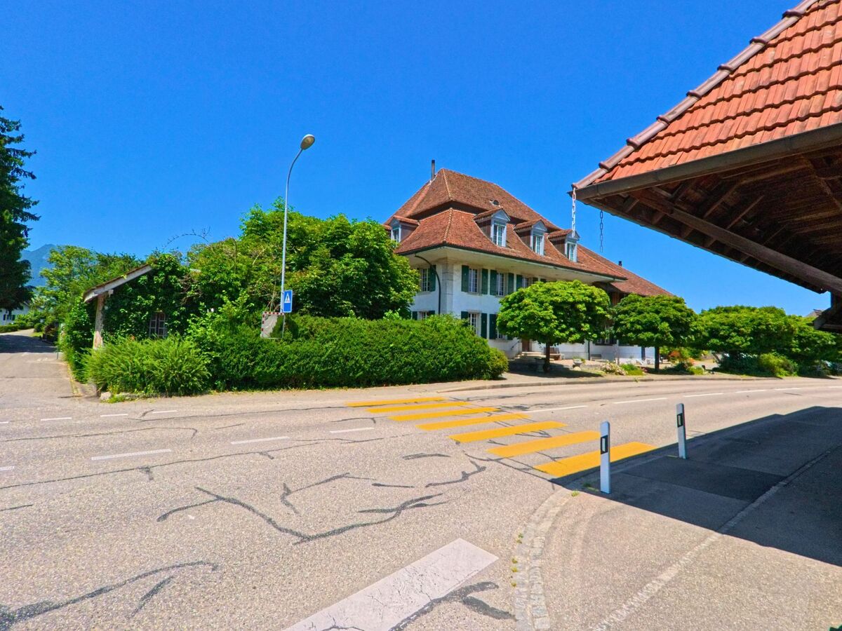 In Lüsslingen-Nennigkofen (4574, Kanton Solothurn) liegt ein markantes, helles Gebäude mit Mansarddach an einer Kreuzung mit Fussgängerstreifen im Dorfzentrum.