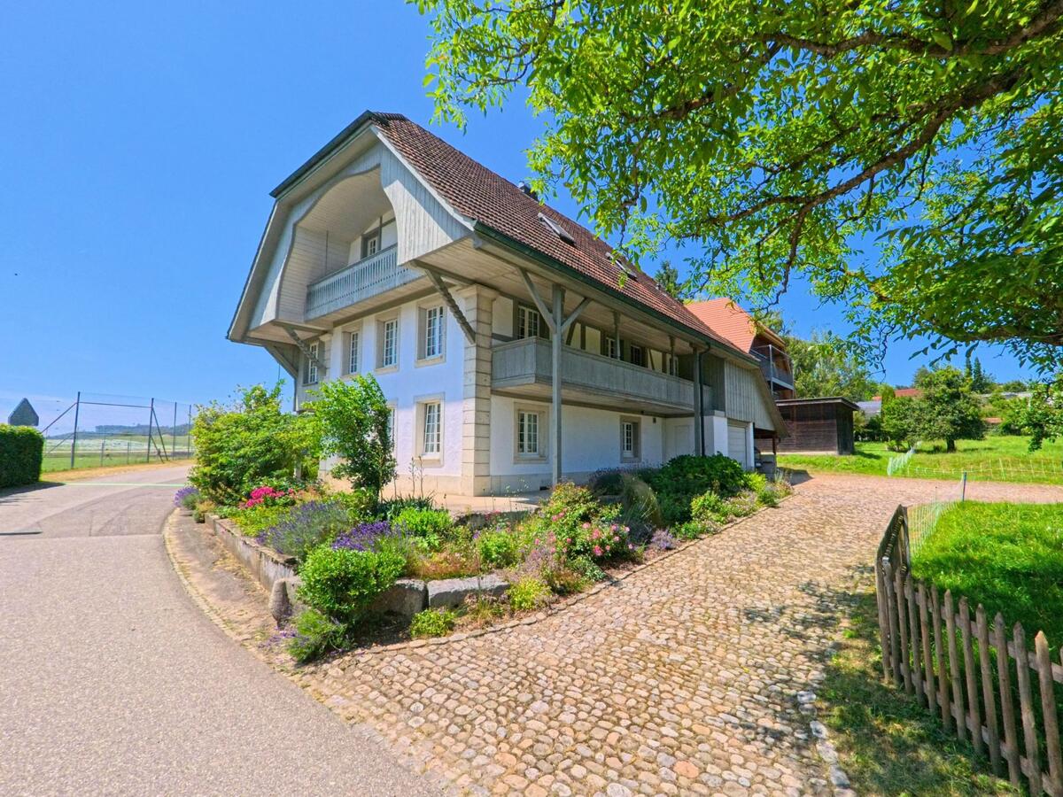 In Lüterkofen-Ichertswil (4571, Kanton Solothurn) steht ein helles Bauernhaus mit schönem Vorgarten an einem gepflasterten Weg nahe freiem Feld.