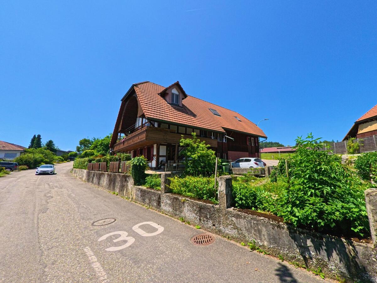 In einer Tempo-30-Zone von Lüterkofen-Ichertswil (4571, Kanton Solothurn) steht ein traditionelles Haus mit markantem Dachgiebel und Vorgarten an einer leicht ansteigenden Strasse.