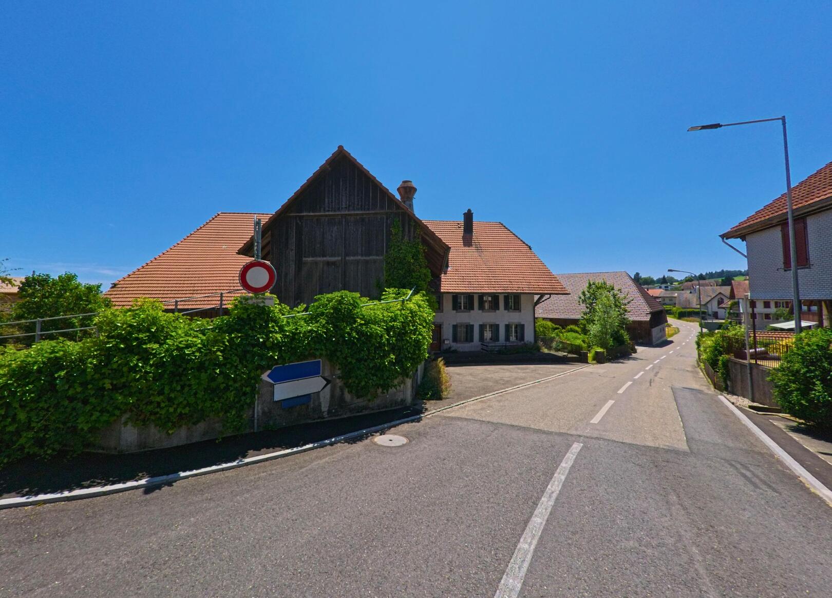 In Lüterswil-Gaechliwil (4584, Kanton Solothurn) zweigt eine schmale Strasse zwischen traditionellen Bauernhaeusern mit roten Daechern ab.