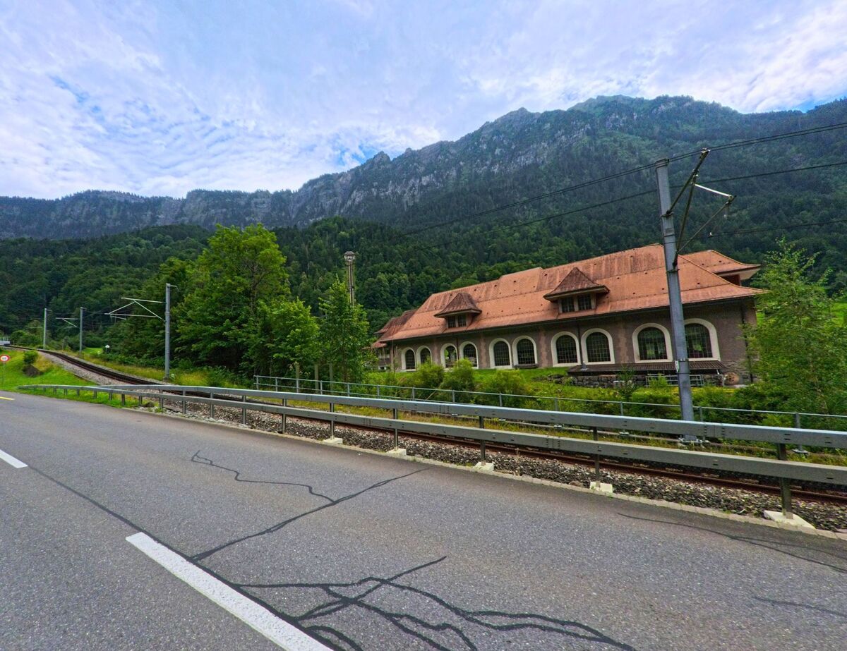 Entlang der Bahnlinie in Lütschental (3816, Kanton Bern) steht ein langgestrecktes Gebäude mit roten Dachziegeln vor dicht bewaldeten Berghängen.