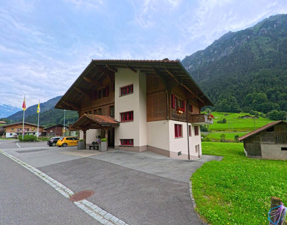 Das Gemeindehaus von Lütschental (3816, Kanton Bern) steht vor einer Kulisse aus grünen Wiesen und bewaldeten Hängen am Rand einer ruhigen Strasse.