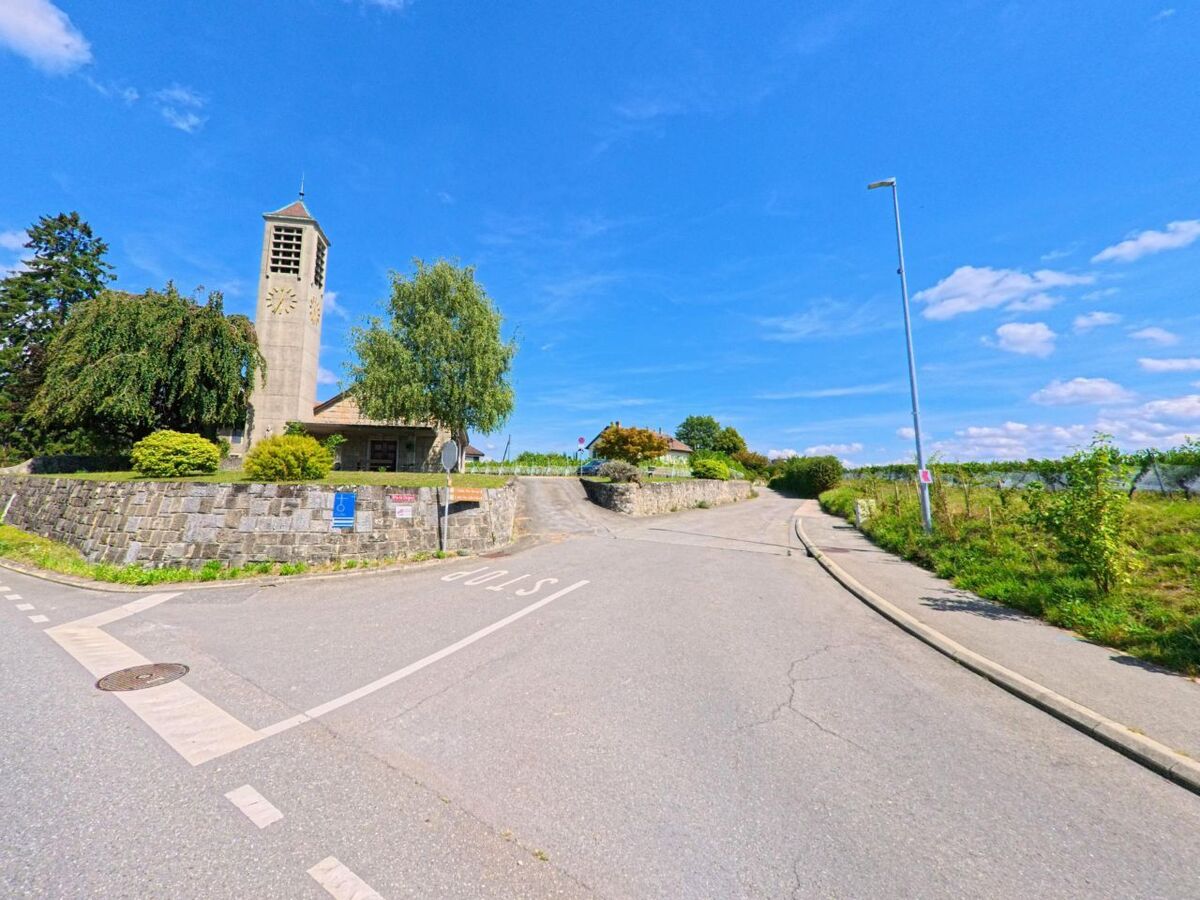 Die Kirche von Lully (1132, Kanton Waadt) mit ihrem markanten Glockenturm steht oberhalb einer Strasse und ist von Gruen umgeben.