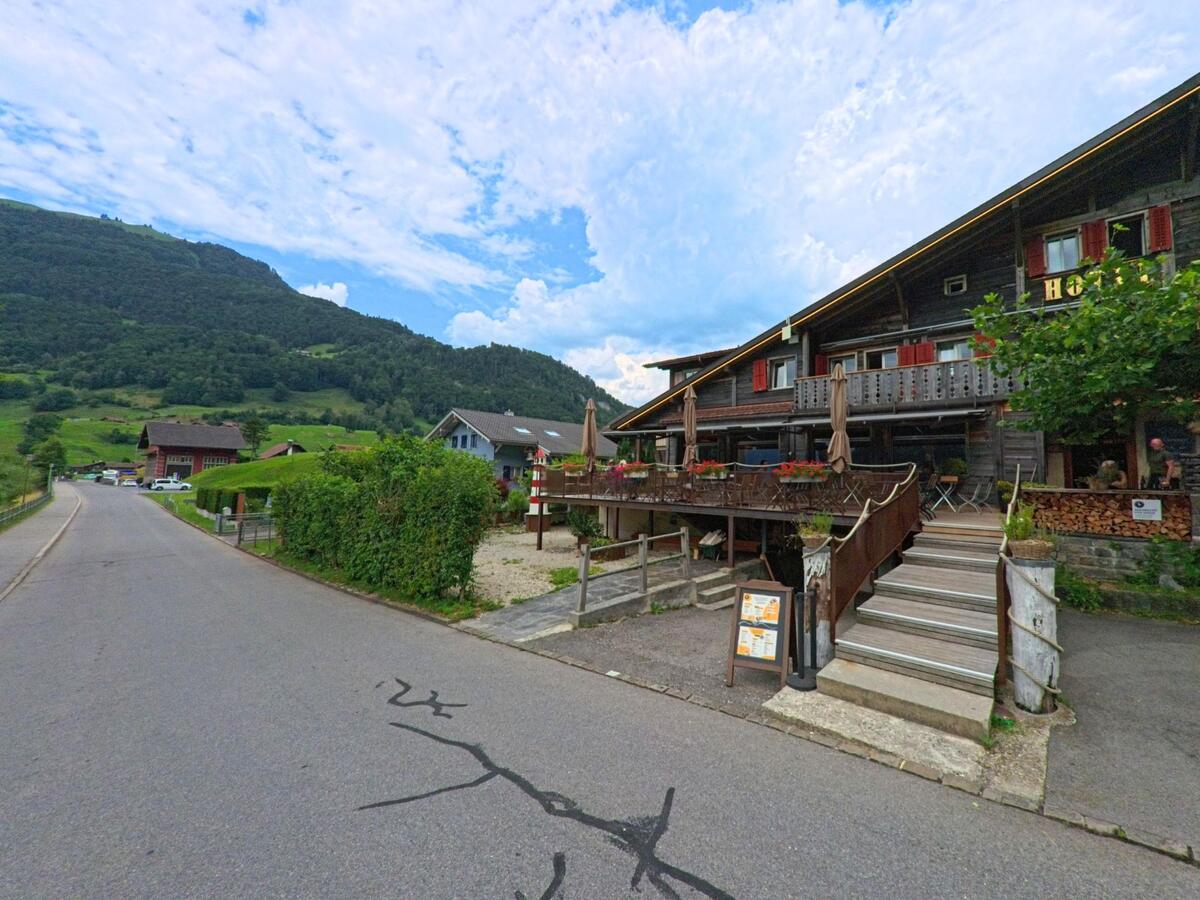 Ein Hotel mit gemütlicher Holzveranda und roter Fensterläden steht in Lungern (6078, Kanton Obwalden) an einer ruhigen Strasse mit Blick auf die grüne Hügellandschaft.