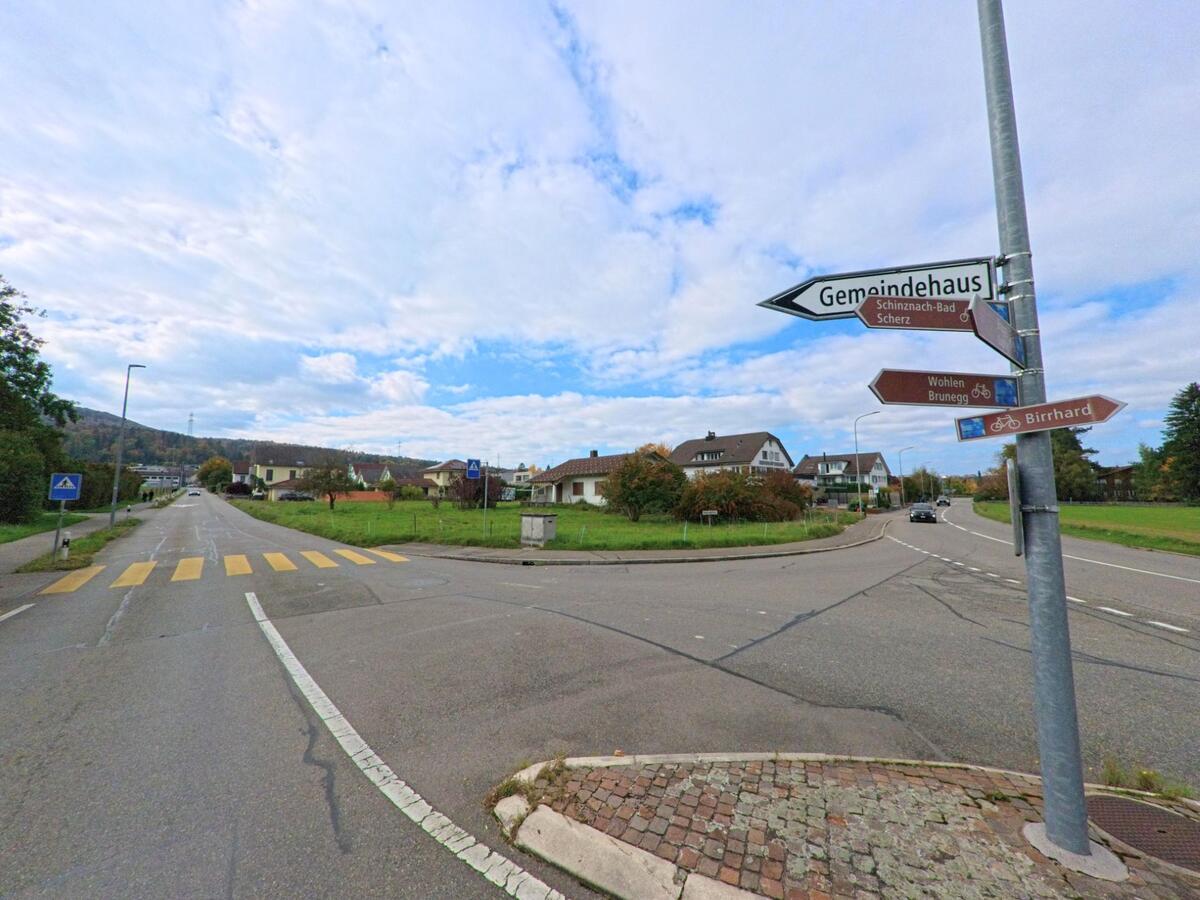 An einer Kreuzung in Lupfig (5242, Kanton Aargau) zeigen Wegweiser den Weg zum Gemeindehaus sowie zu umliegenden Orten wie Birrhard, Scherz und Wohlen.