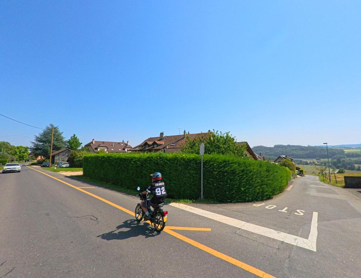Ein Kind auf einem Fahrrad faehrt in Lussery-Villars (1307, Kanton Waadt) eine Strasse entlang, die vorbei an Wohnhaeusern in die Landschaft fuehrt.