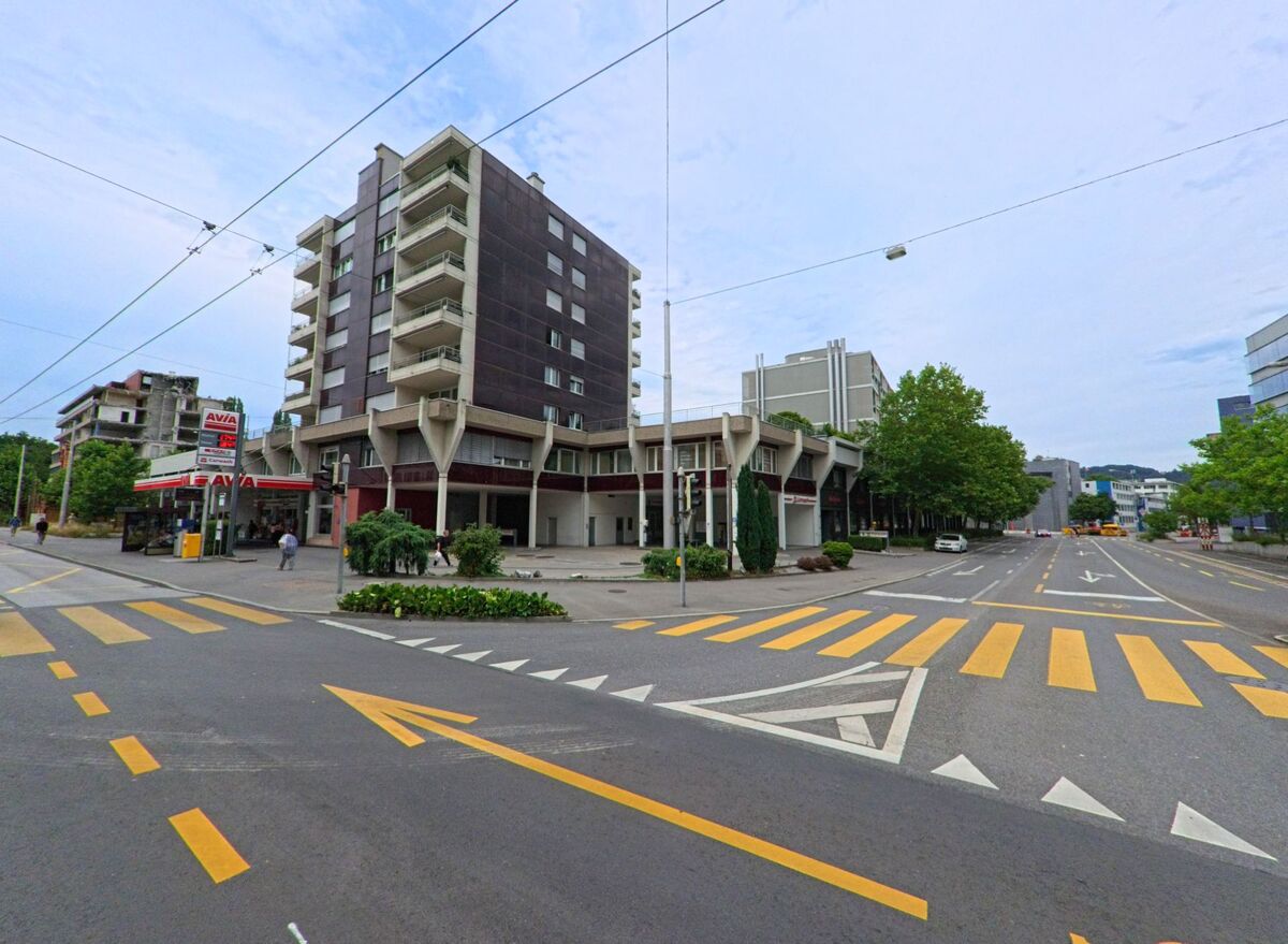 Ein markantes Eckgebaeude mit Tankstelle praegt die Kreuzung in Luzern (6005, Kanton Luzern), wo breite Fahrbahnen, Zebrastreifen und Verkehrsschilder das urbane Stadtbild bestimmen.