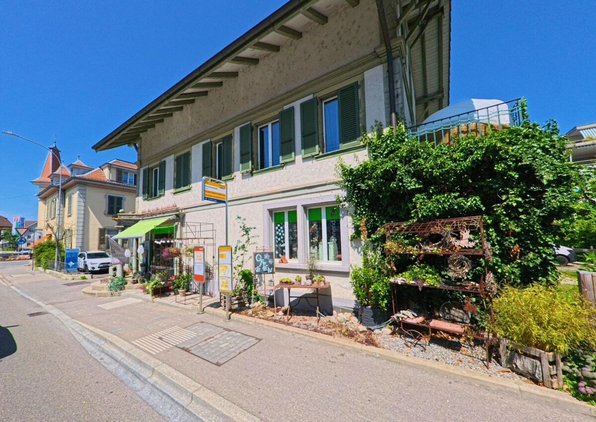 In Lyss (3250 im Kanton Bern) befindet sich eine charmante Bushaltestelle vor einem Haus mit gruenen Fensterlaeden und einem liebevoll dekorierten Geschaeft.