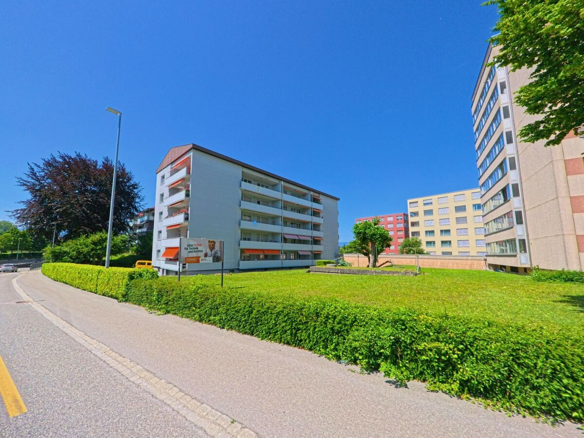 n Lyss (3250 im Kanton Bern) stehen mehrere Wohnhochhaeuser mit Balkonen und orangefarbenen Markisen rund um eine begruente Freiflaeche.