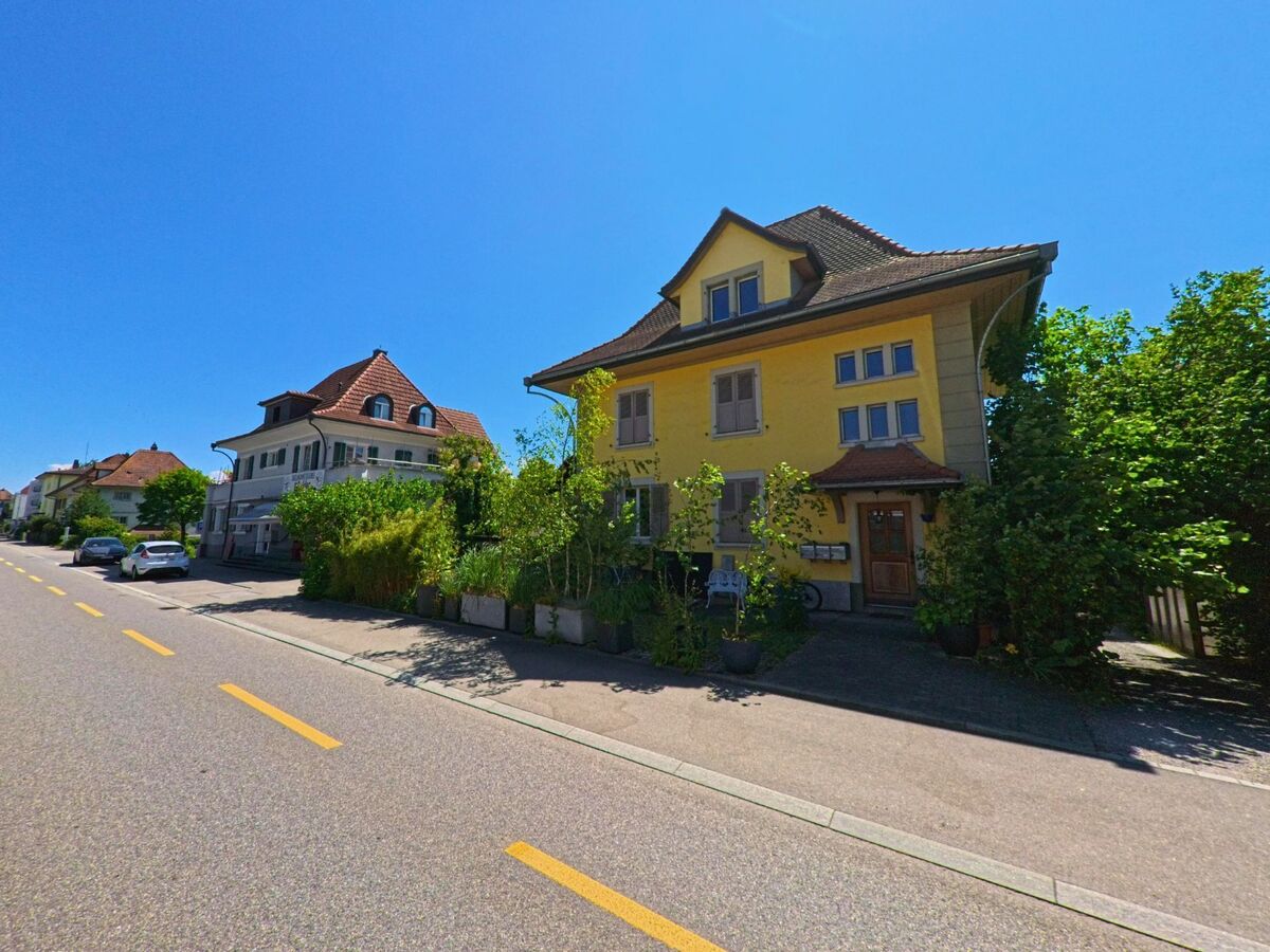 In Lyss (3250, Kanton Bern) reihen sich entlang einer sonnigen Strasse gepflegte Wohnhaeuser mit Vorgarten und historischer Architektur.