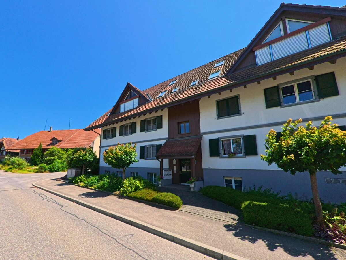 In Lyss (3292, Kanton Bern) säumen gepflegte Mehrfamilienhäuser mit Fensterläden und Vorgärten eine ruhige Quartierstrasse.