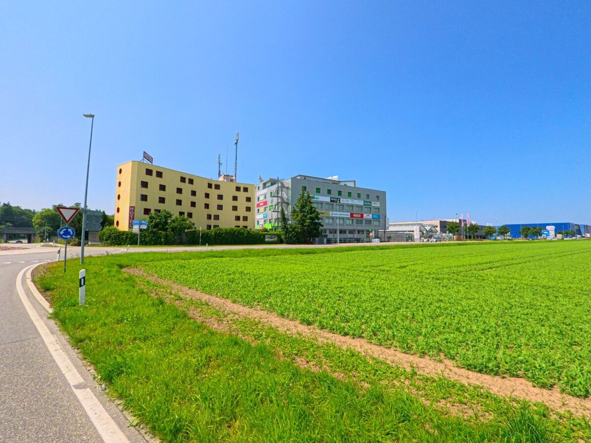 In Lyssach (3421, Kanton Bern) liegen ein Hotel und mehrere Geschäftshäuser mit Werbetafeln direkt an einem Kreisel am Übergang von Feldern zur Gewerbezone.