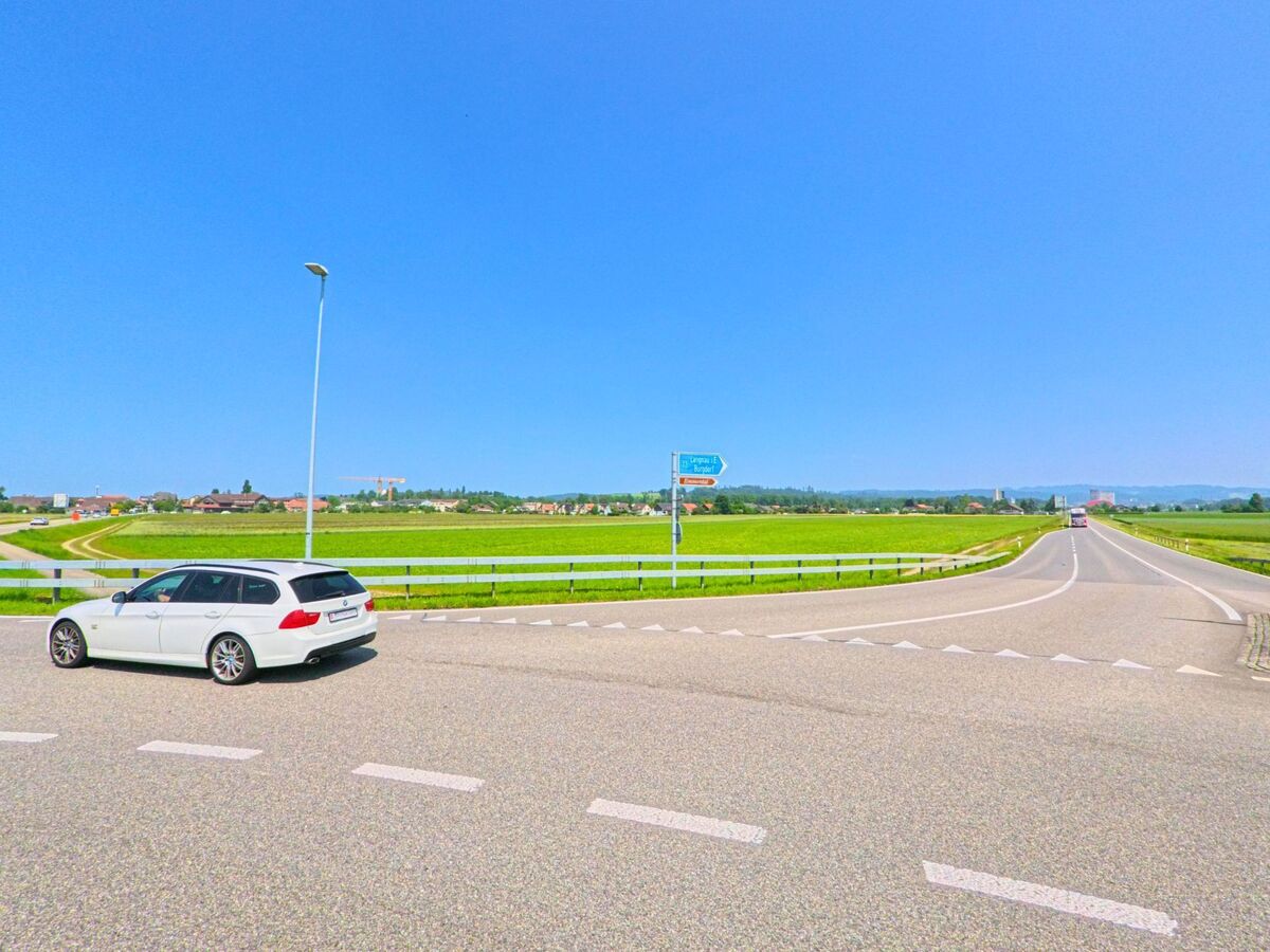 Am Ortsrand von Lyssach (3421, Kanton Bern) zweigt eine Landstrasse mit Wegweiser zwischen weiten Feldern in Richtung Burgdorf und Kirchberg ab.
