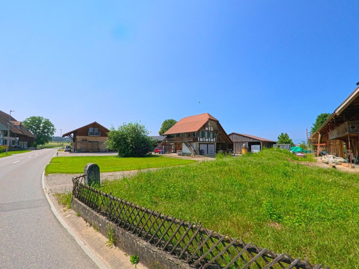  In Lyssach (3421, Kanton Bern) stehen mehrere landwirtschaftlich genutzte Gebäude und Werkstätten entlang einer ruhigen Strasse mit Blick auf offene Felder.