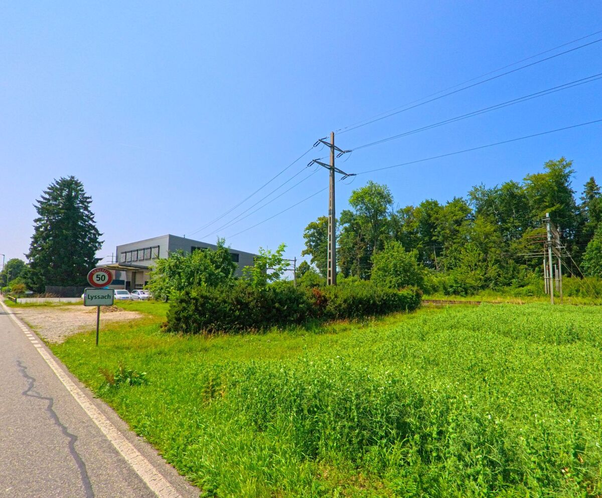 Am Ortseingang von Lyssach (PLZ 3421, Kanton Bern) steht ein Geschwindigkeitsschild neben einer Strasse, die an Feldern, Stromleitungen und Gewerbebauten vorbeiführt