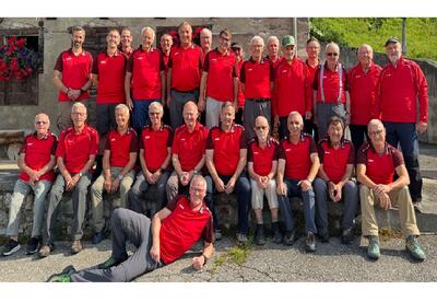 Die Männerriege Flums aus Flums (8890, Kanton St. Gallen) posiert in roten Sportshirts für ein Gruppenfoto in einer sonnigen, idyllischen Umgebung.