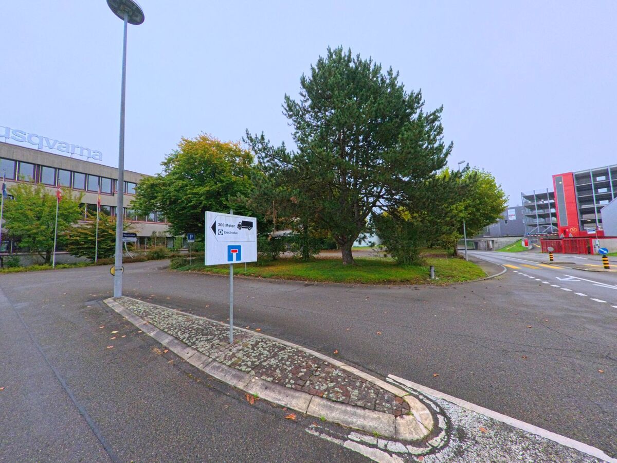 Am Rand des Industriegebiets von Mägenwil (5506, Kanton Aargau) steht ein Firmengebäude mit grossem Baum und Wegweiser in Richtung Electrolux und Parkhaus.