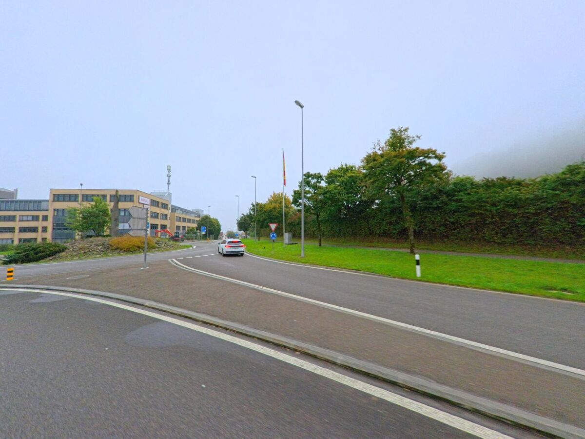 Ein Auto fährt auf eine grosszügige Strassenkreuzung in Mägenwil (5506, Kanton Aargau) zu, umgeben von modernen Bürogebäuden und gepflegten Grünflächen.