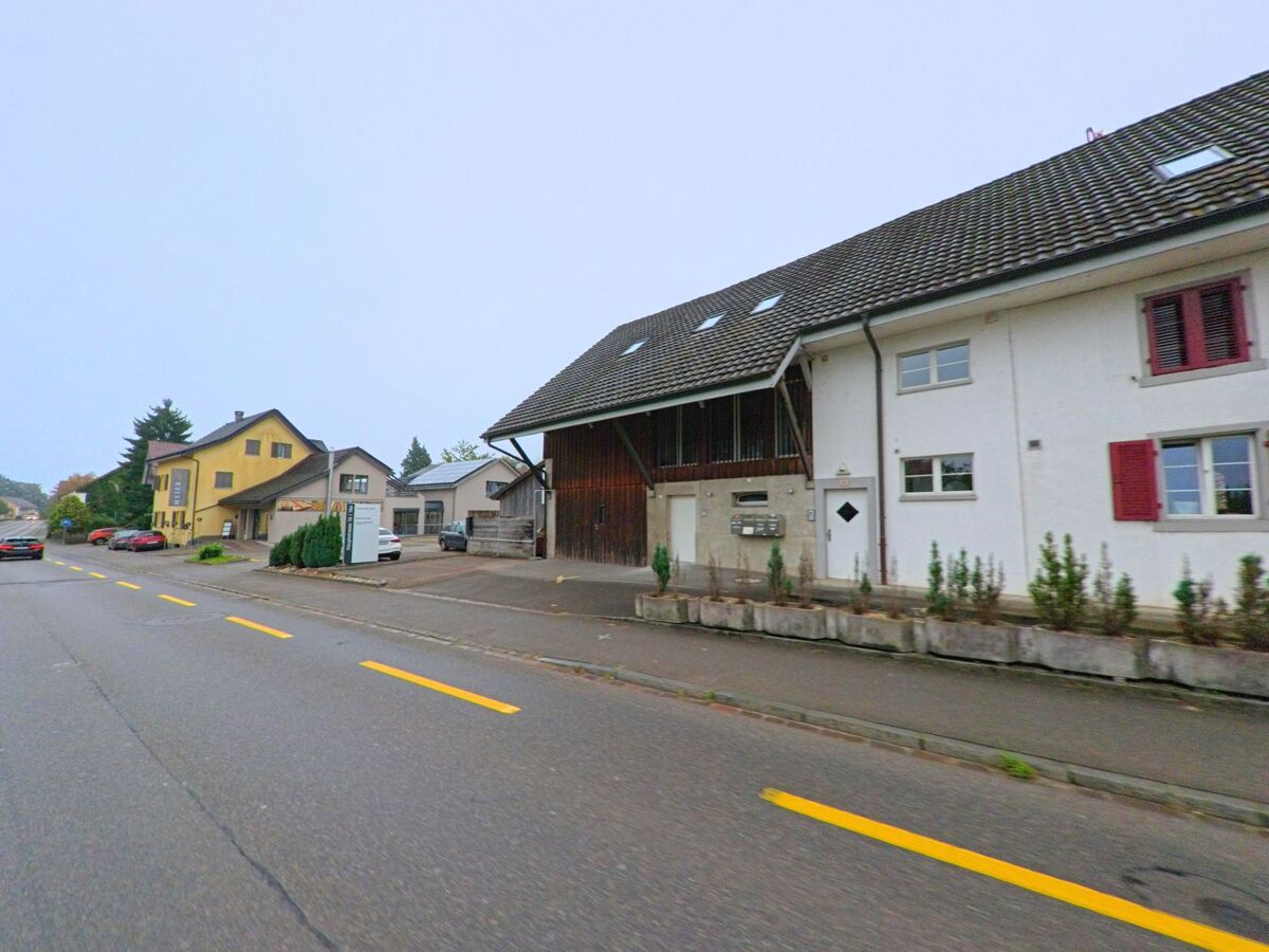Mehrere Wohnhäuser mit unterschiedlichen Fassaden stehen entlang der Hauptstrasse in Mägenwil (5506, Kanton Aargau), im Vordergrund ein umgebautes Bauernhaus mit Scheunenteil.