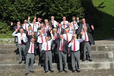 Der Maennerchor Frohsinn steht in Oberuzwil (9242) im Kanton St. Gallen auf Treppen und hebt bei Sonnenschein die Haende zum Gruss.