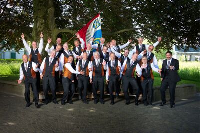 Der Männerchor Pfaffnau in Pfaffnau (6264, Kanton Luzern) posiert mit einer Fahne und in festlicher Kleidung vor einem Baum für ein fröhliches Gruppenfoto.