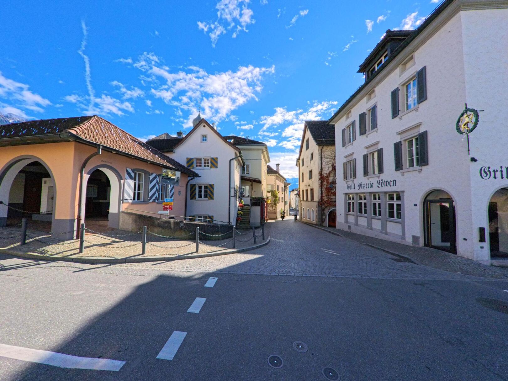 Zwischen historischen Häusern mit verzierten Fassaden öffnet sich eine gepflasterte Altstadtgasse in Maienfeld (7304, Kanton Graubünden) unter einem klaren Himmel.