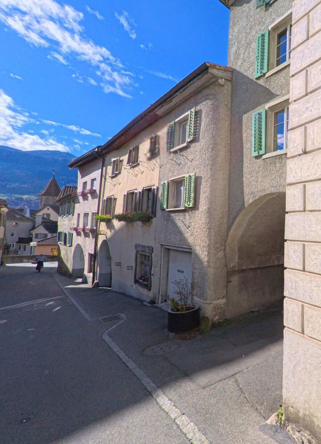 Entlang einer schmalen Gasse mit historischen Wohnhäusern und Rundbögen zeigt sich ein stiller Altstadtbereich von Maienfeld (7304, Kanton Graubünden) mit Blick auf die umliegenden Hänge.