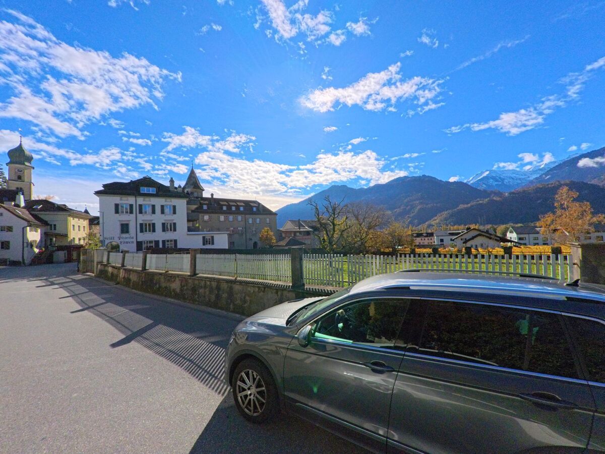 Entlang einer ruhigen Strasse eröffnet sich der Blick auf historische Gebäude und eine umzäunte Grünfläche in Maienfeld (7304, Kanton Graubünden), eingerahmt von Bergen unter leicht bewölktem Himmel.