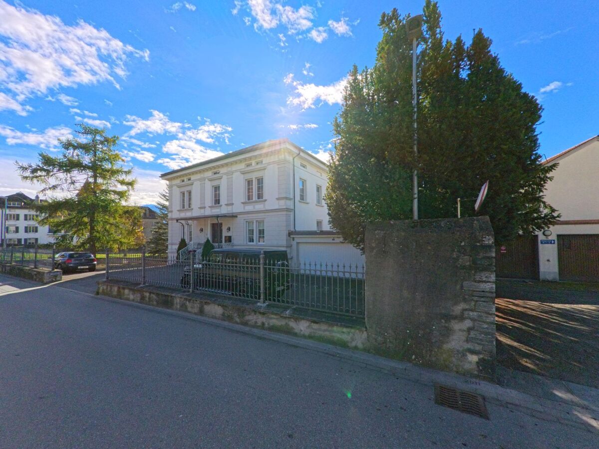 An einer ruhigen Strasse steht eine repräsentative Villa mit eingefriedetem Garten in Maienfeld (7304, Kanton Graubünden), umgeben von Bäumen und weiterer Wohnbebauung.