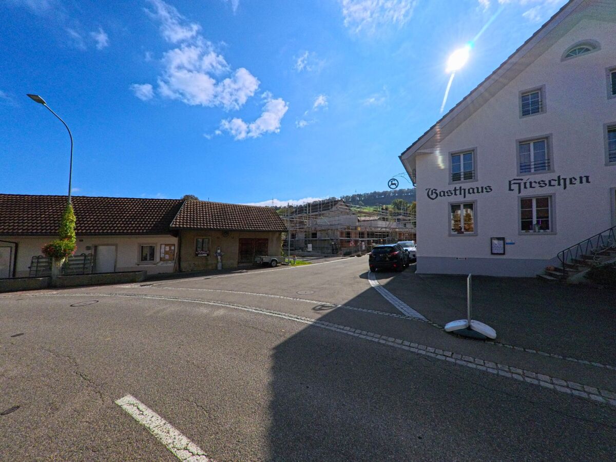 Das Gasthaus Hirschen in Mandach (5318, Kanton Aargau) liegt an einer Strassenecke im Dorfzentrum, neben weiteren Gebäuden mit roten Ziegeldächern.