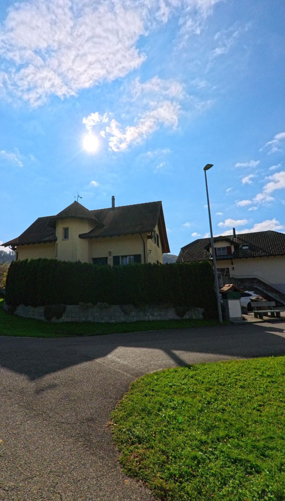 Ein gelbes Wohnhaus mit markantem Eckturm steht in Mandach (5318, Kanton Aargau) an einer kleinen Strassenkreuzung unter strahlend blauem Himmel.