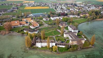 In Münsterlingen (8596, Kanton Thurgau) liegt eine Anlage am See mit mehreren Gebaeuden, Gruenflaechen und Wegen zwischen Wasser und Siedlung.