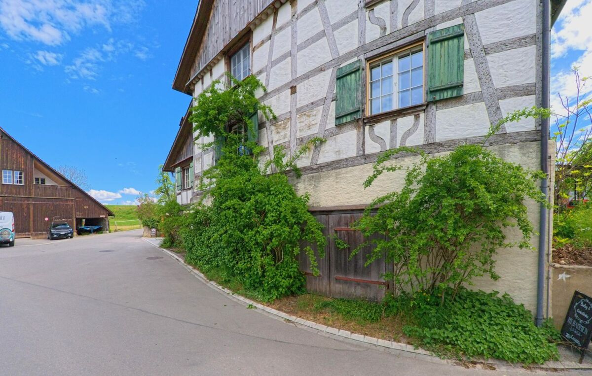 Im PLZ-Gebiet 8460 der Gemeinde Marthalen im Kanton Zürich steht ein historisches Fachwerkhaus mit grünem Fensterladen und dichter Begrünung an einer ruhigen Nebenstrasse.