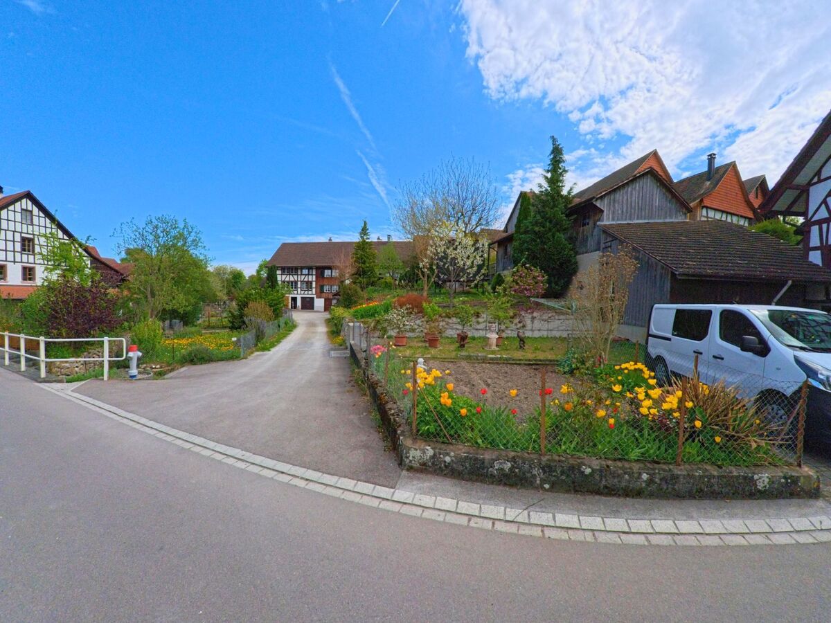 In Marthalen im Kanton Zürich mit der PLZ 8460 führt ein schmaler Weg durch gepflegte Gärten mit bunten Blumenbeeten hin zu einem traditionellen Fachwerkhaus.