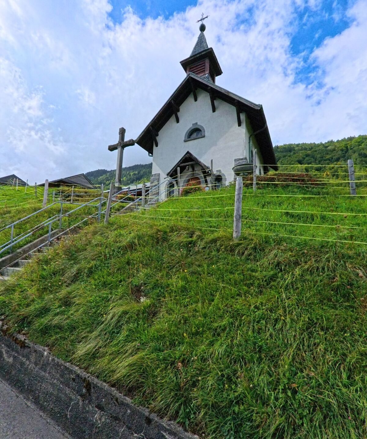 Eine kleine Kapelle mit Turm und Holzkreuz steht in Massongex (1869, Kanton Wallis) auf einem Gruenhuegel am Dorfrand.
