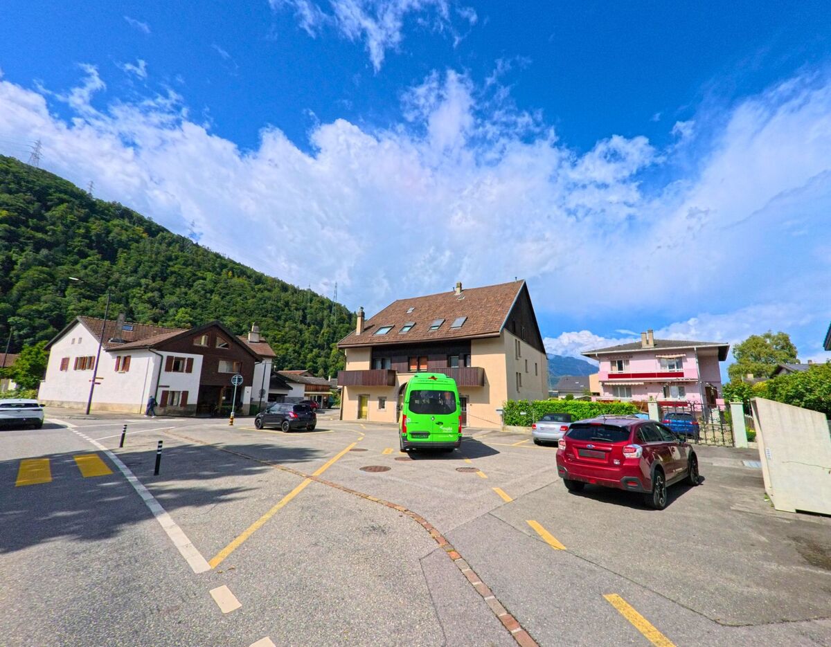 Wohnhaeuser mit Satteldaechern stehen in Massongex (1869, Kanton Wallis) an einer Kreuzung mit Zebrastreifen und parkenden Autos.