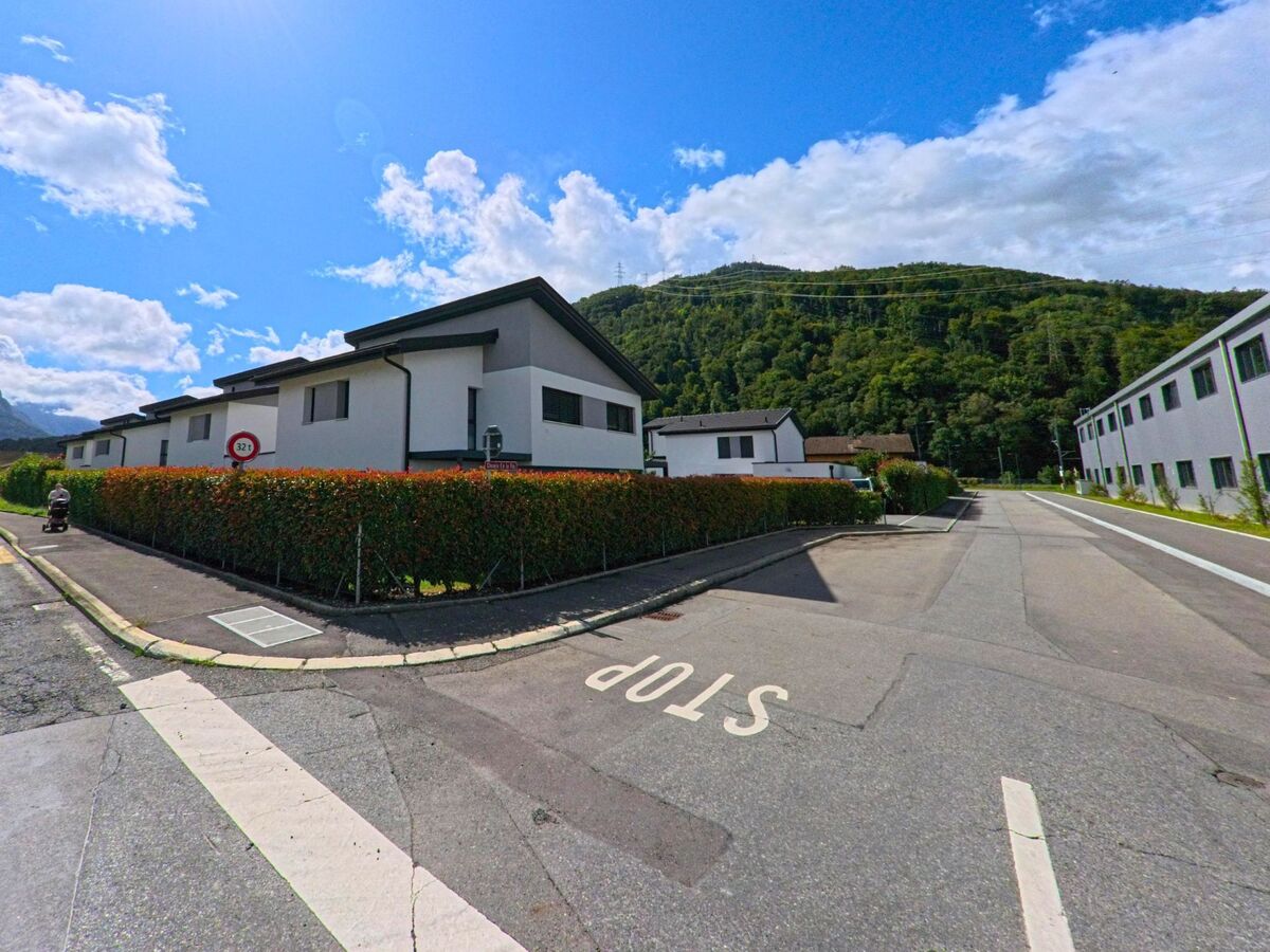 Neue Wohnsiedlungen mit weissen Fassaden praegen in Massongex (1869, Kanton Wallis) eine ruhige Strasse am Waldrand.