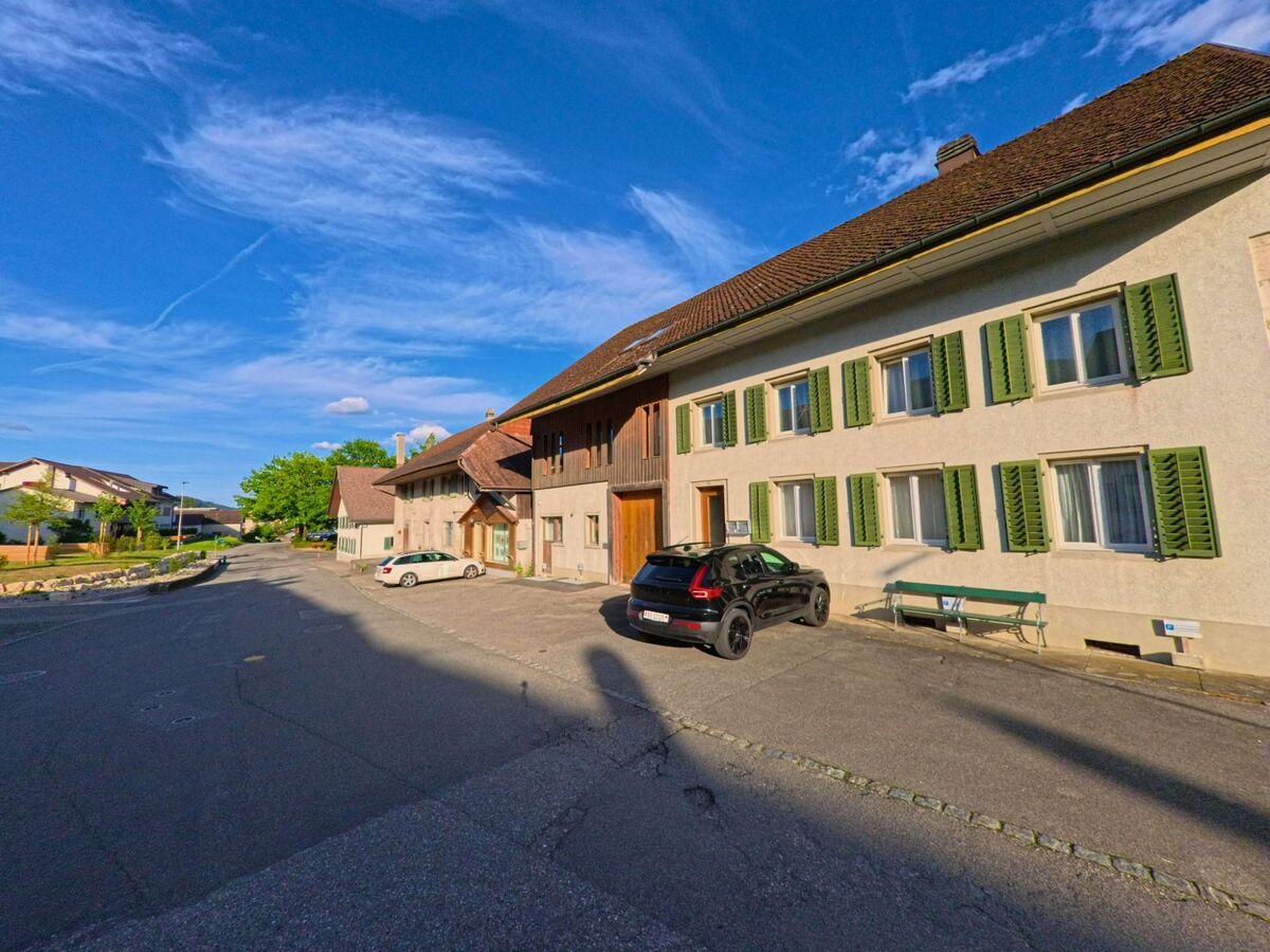 Eine Häuserzeile mit grünen Fensterläden und parkenden Autos säumt in Matzendorf (4713, Kanton Solothurn) eine breite Quartierstrasse.