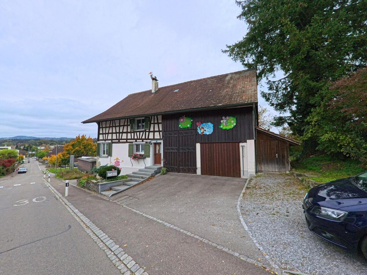 An einer leicht abfallenden Strasse in Matzingen (9548, Kanton Thurgau) steht ein Fachwerkhaus mit grossem Scheunentor und dekorierten Holzwänden.